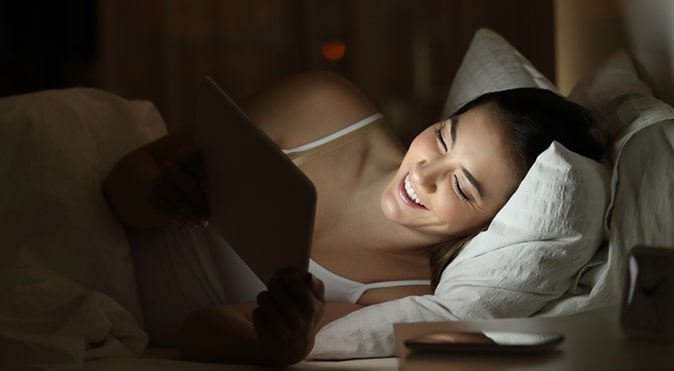 Young woman laying in bed with iPad, Better Sleep Council
