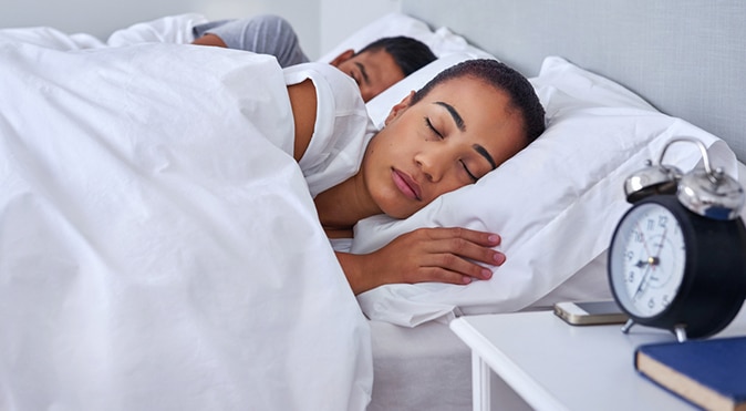Couple sleeping in bed with alarm clock on bedside table, Better Sleep Council
