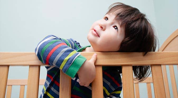 Young toddler standing inside crib, Better Sleep Council