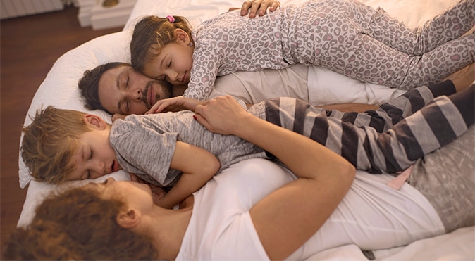 Mother, Father, and two children asleep in bed together, Better Sleep Council
