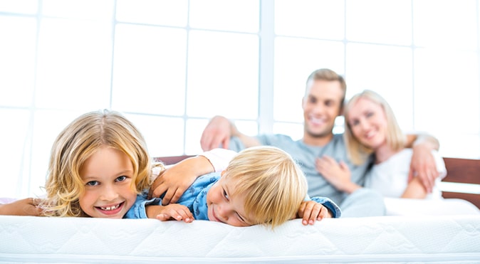 2 young children and parents sitting on mattress, Better Sleep Council