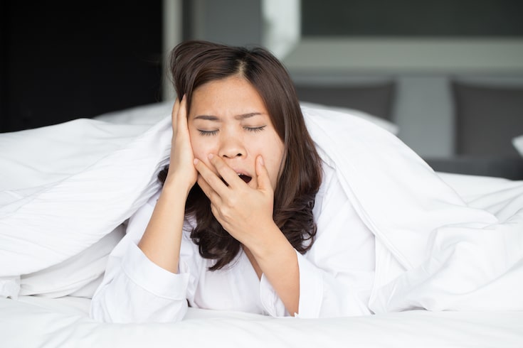 Woman yawning under white covers in bed, Better Sleep Council