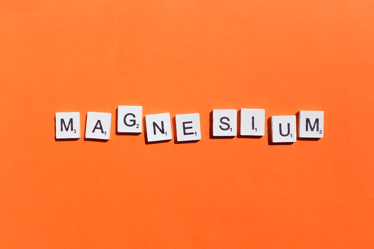 letters from the Scrabble board game spell out the word magnesium on a solid orange background
