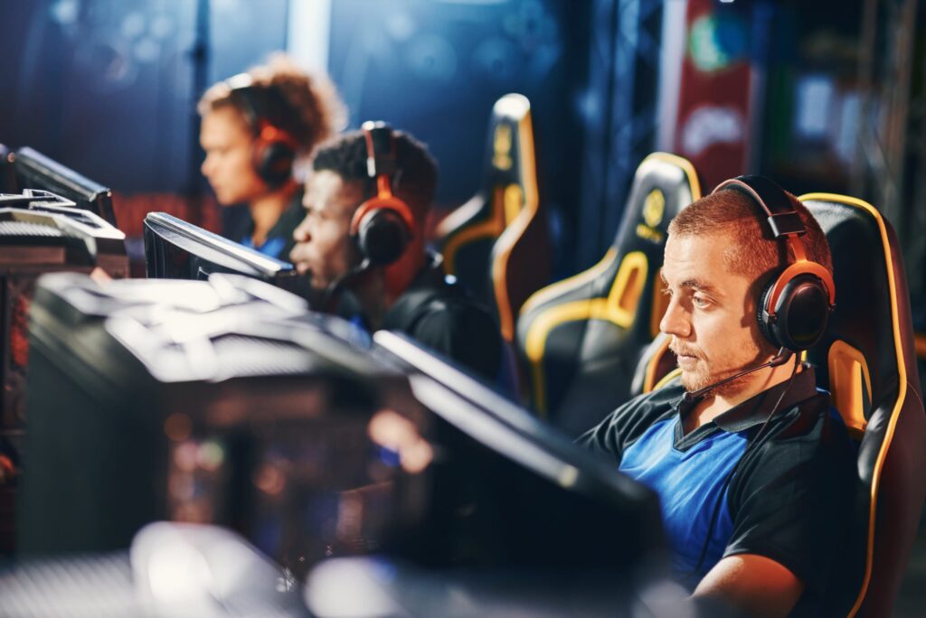Focused on game. Male cybersport gamer wearing headphones playing online video games, participating in eSport tournament, blurred team members on the background