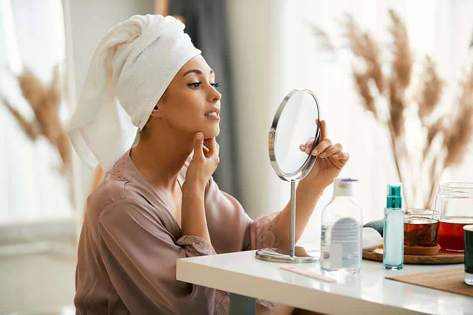 Young beautiful woman looking at her face skin in a mirror at home.