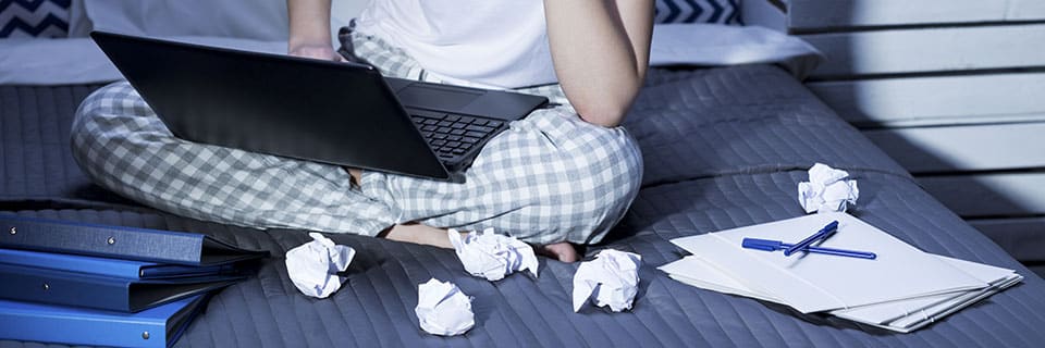 Woman in pajamas sitting in bed and working on laptop at night