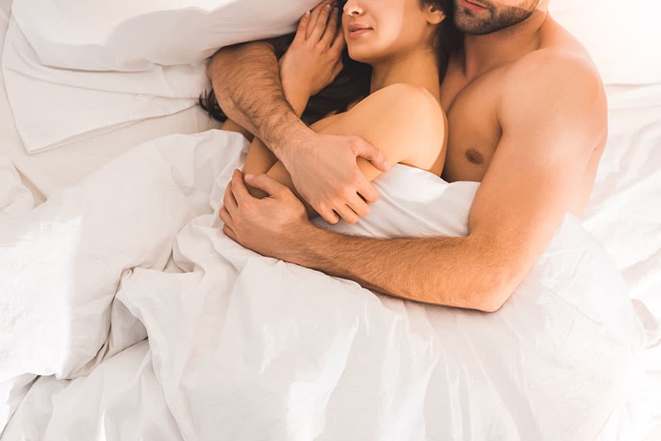 cropped view of nude couple embracing while sleeping in bed