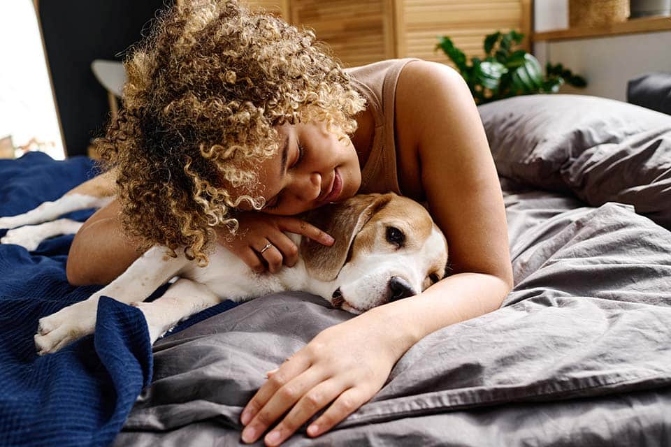 woman with curly hair hugging with her lovely dog on bed in bedroom