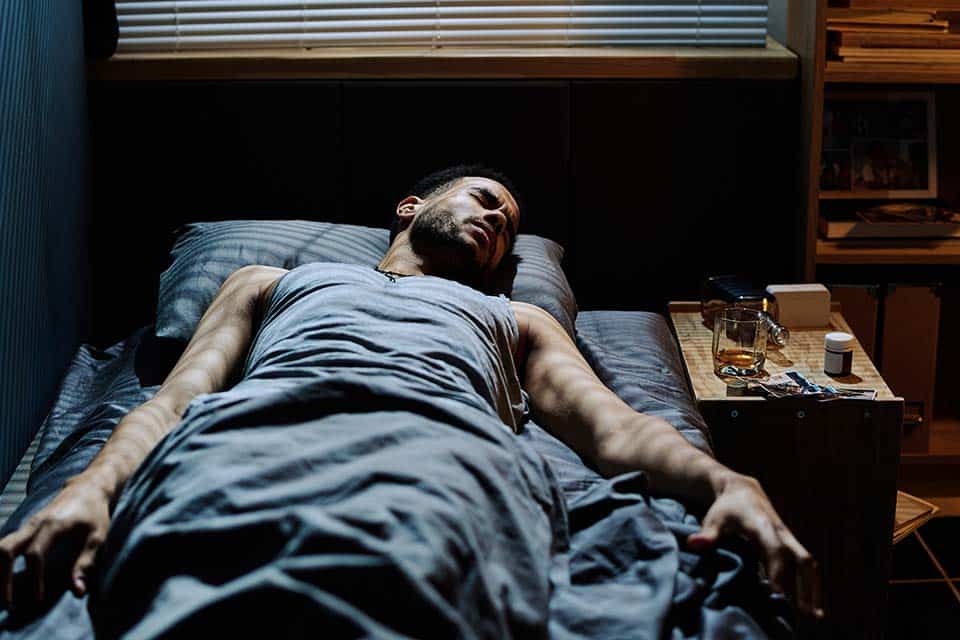 Young man lying on bed by night table