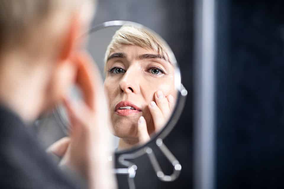 Skin Aging Concept. Middle-Aged Lady Looking In Round Mirror At facial Wrinkle Touching Face Standing In Bathroom Indoors. Selective Focus