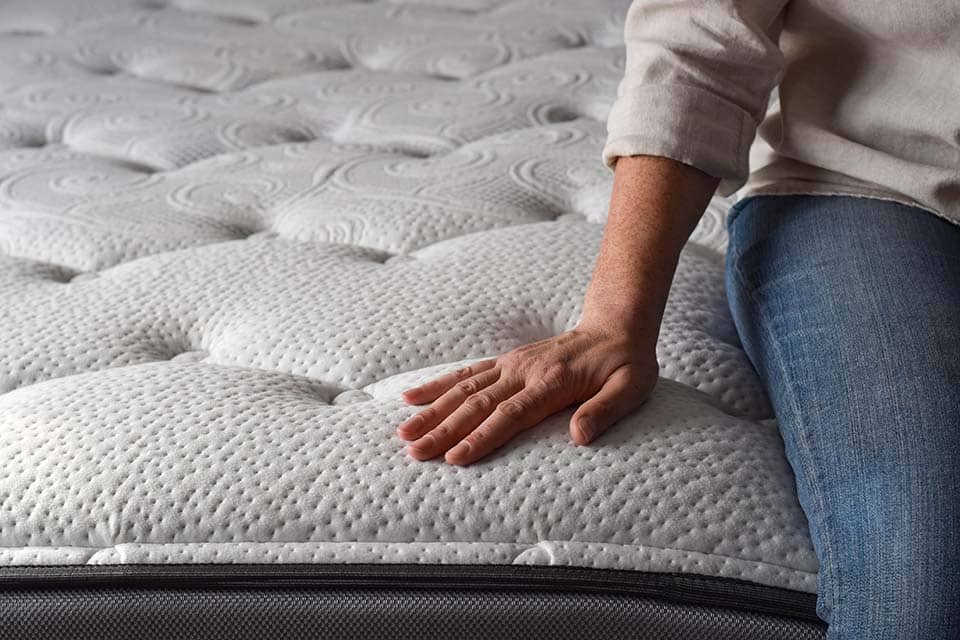 Woman sitting on a brand new mattress and touching the fabric with copy space