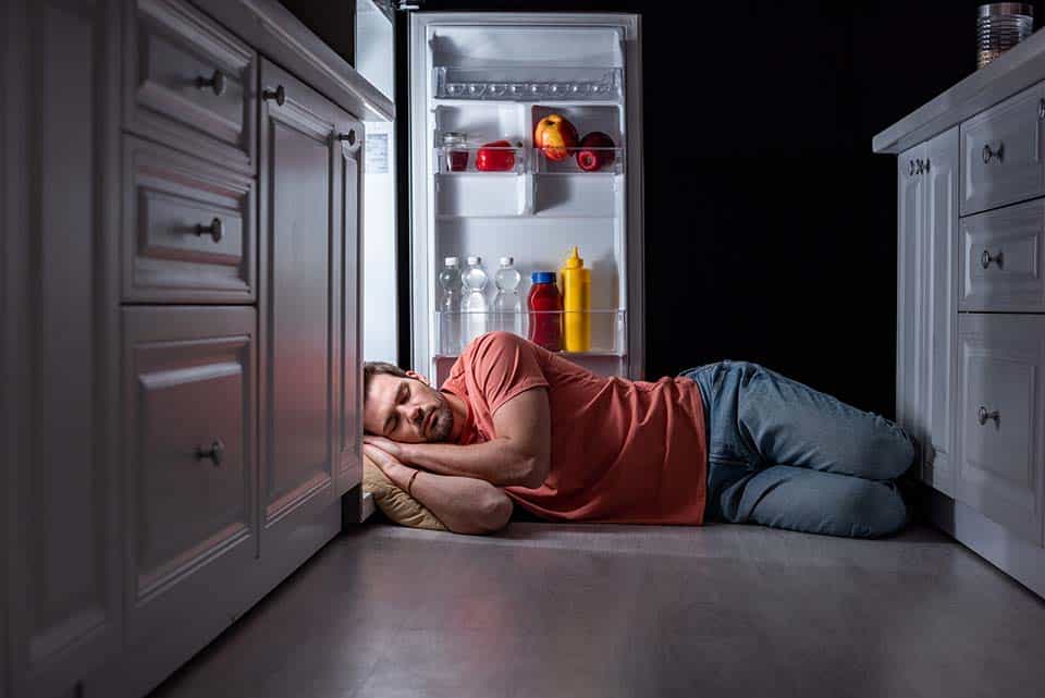 exhausted man sleeping near open refrigerator on kitchen floor