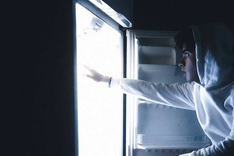 a young man reaching into a refrigerator at night