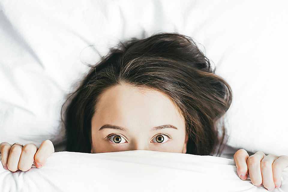 Woman hiding under covers out of fear of bed bugs