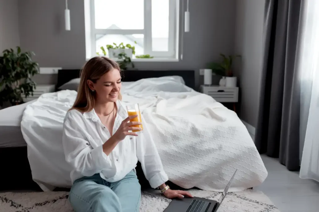 girl sits floor bedroom use laptop remote work drink orange juice 1